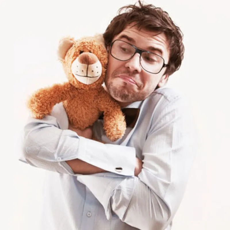 A man in glasses pulling a face while hugging a teddy bear