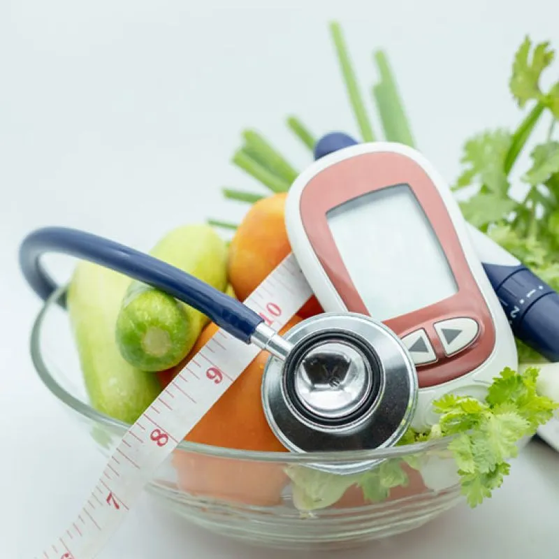 A bowl of vegetables with a stethoscope, tape measure and blood glucose meter