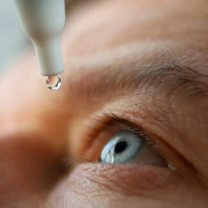 A drop falling from an eye-drop bottle into an open eye