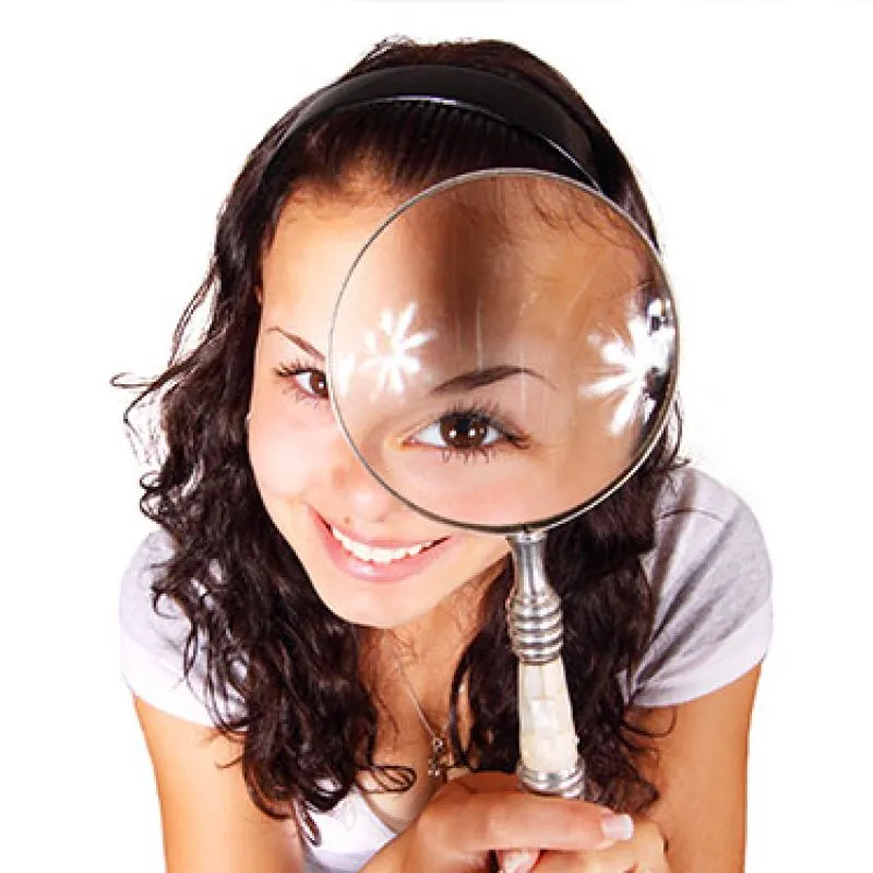 A young woman smiling through a magnifying glass held over one eye