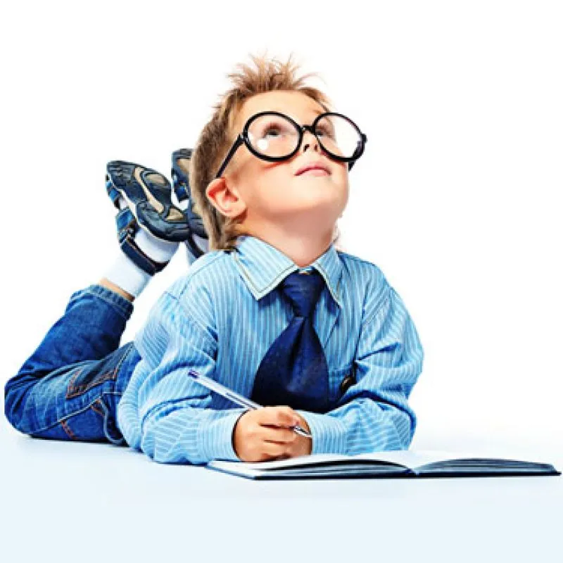 A young boy in round glasses lying on the floor writing in a notebook