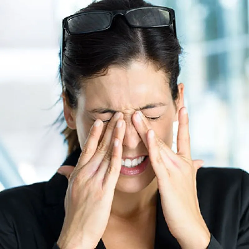 A woman with her glasses pushed up, rubbing both eyes